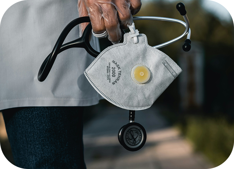 Mão de um médico de jaleco segurando um estetoscópio e uma máscara PFF2